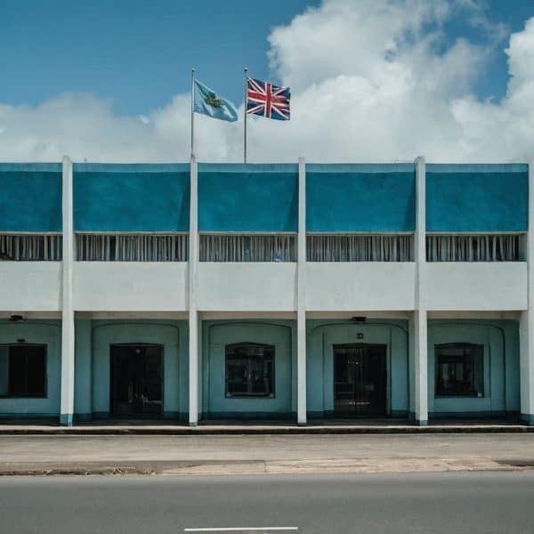 Fiji government building with flags, including the Union Jack and Fijian flag, under a cloudy sky.